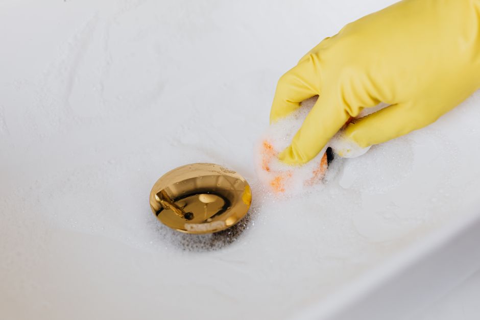 Gloved hand cleaning a clogged bathroom sink drain — professional drain cleaning services in Ceres, CA
