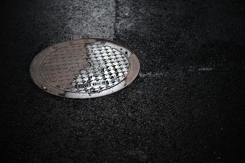 Wet manhole cover on a rain-slicked urban street, representing sewer line infrastructure in Modesto, CA