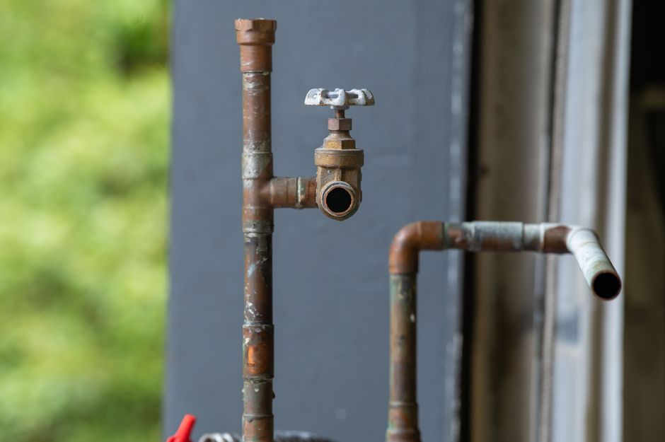 Old rusty copper pipes and shutoff valve on a home exterior, illustrating the need for whole-home repipe service in Lodi, CA