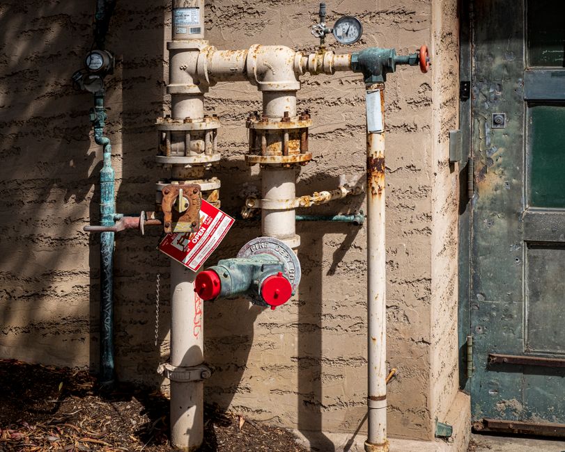 Aging outdoor plumbing pipes and fittings on a California home exterior, illustrating the need for whole-home repipe service in Merced CA